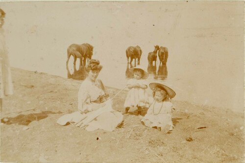 Signora con figlie e cavalli presso una riva